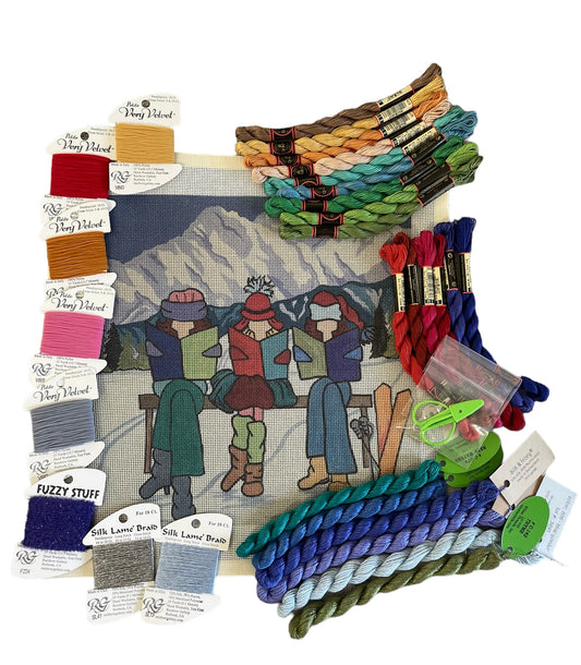 Winter-themed needlepoint kit with skiing figures and a snowy landscape, paired with a selection of colorful threads.